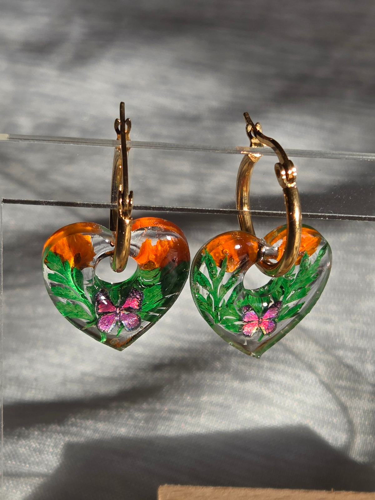 Pampilles en forme de cœurs avec motifs verts et orange, présentées sur des créoles