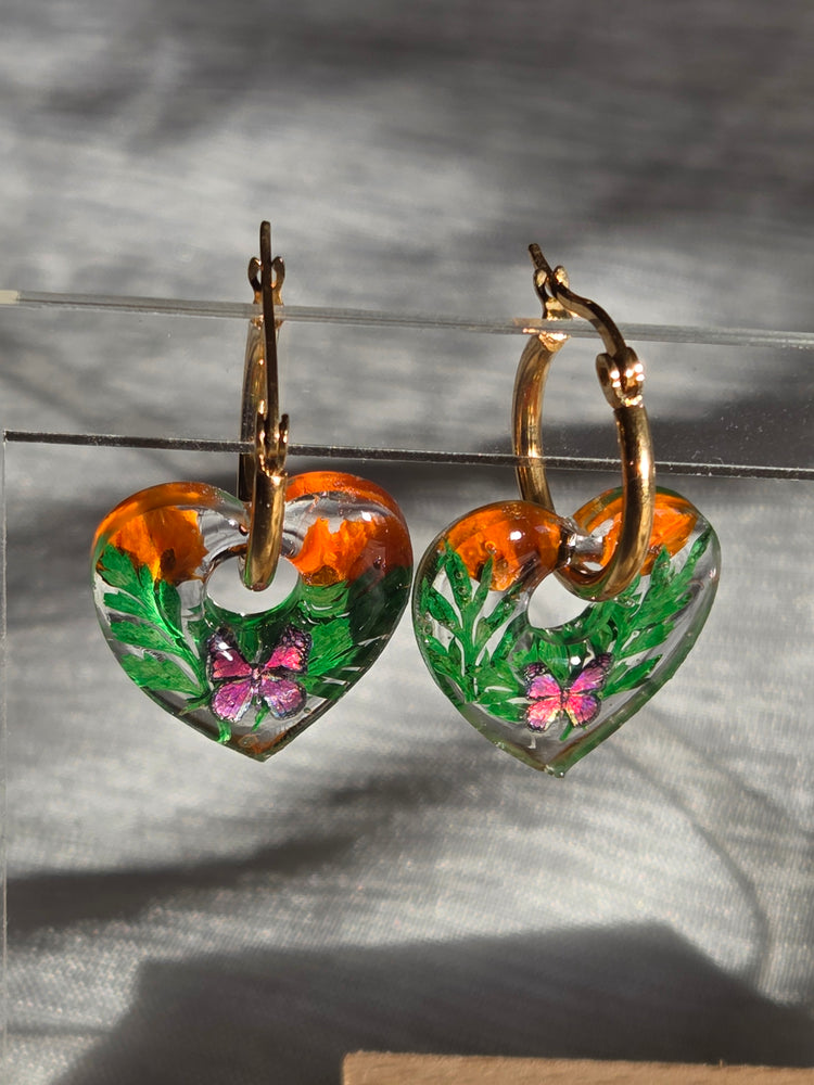 Pampilles en forme de cœurs avec motifs verts et orange, présentées sur des créoles