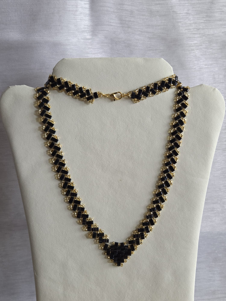 Collier tissé à la main en perles Half Tila noires et rocailles dorées, présenté sur un buste clair