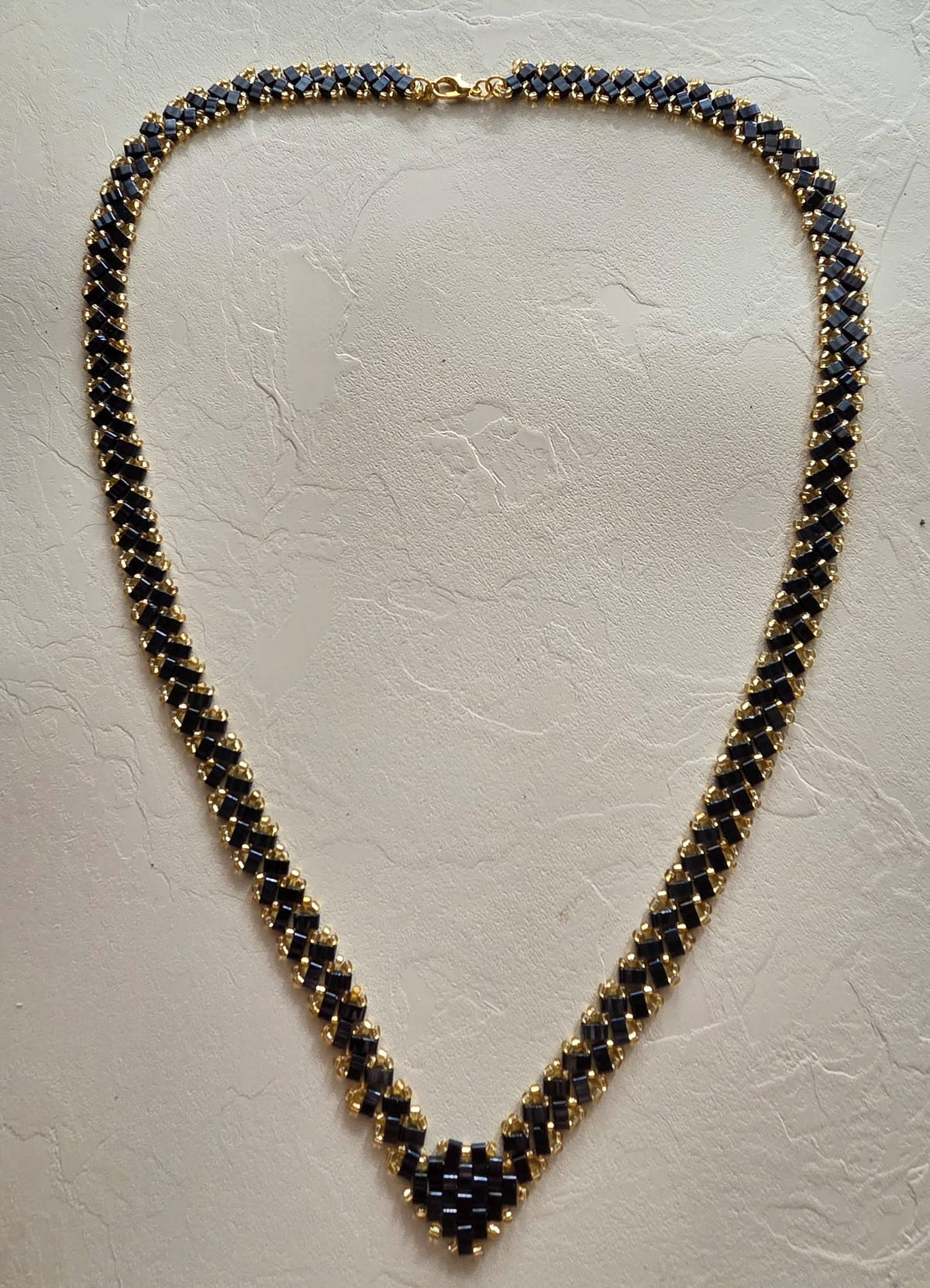 Collier en perles Half Tila noires et rocailles dorées posé à plat, longueur 62 cm et largeur 1 cm